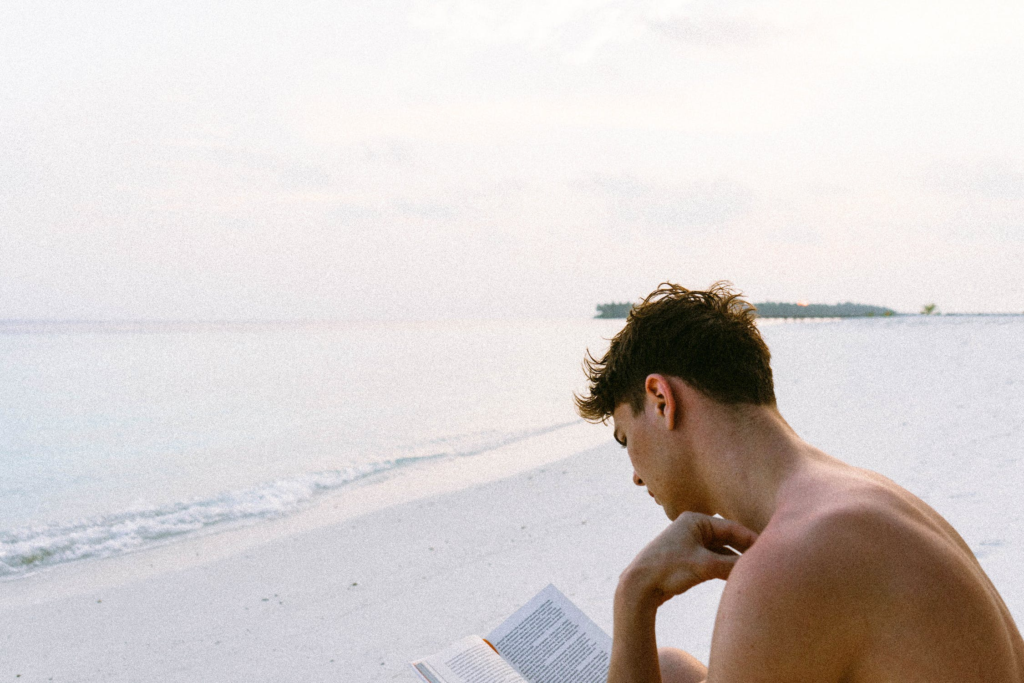 Reading And Learning as a hobby. Picture of a shirtless man reading a book at the beach