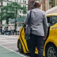 Why Have a Modern Messenger Bag in Transport? black man in stylish suit near taxi