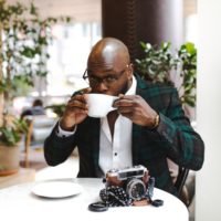 man sitting in front of round table while sipping from white ceramic mug: How to Make Money with Photography in South Africa (Guide)