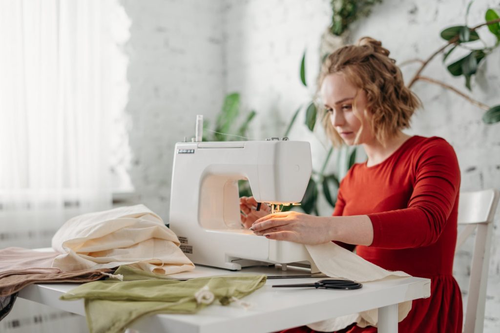woman sewing while sitting on chair: Best Sewing Side Hustles for Beginners + Things to Sell
