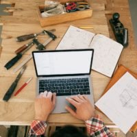 A person using a laptop while on the carpentry workbench: how to make money as a woodworker (full ways & steps)