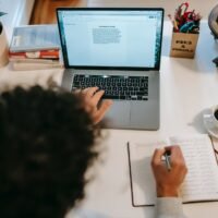 unrecognizable author typing on laptop near coffee at home