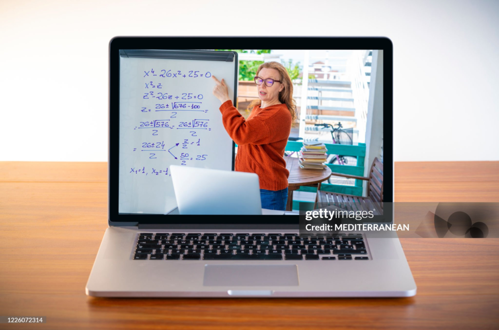 A female teacher teaches remotely via laptop on wood.
